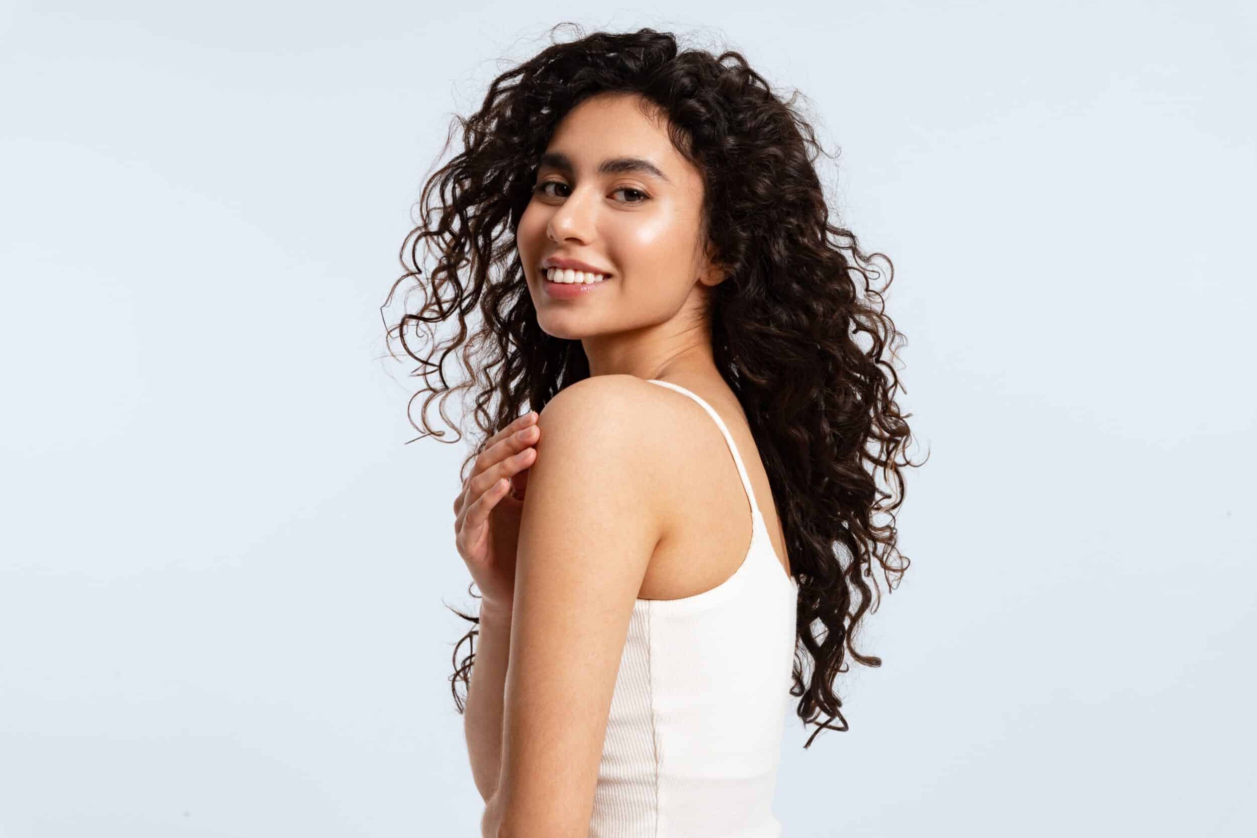 A woman with long dark hair smiling and looking over her shoulder